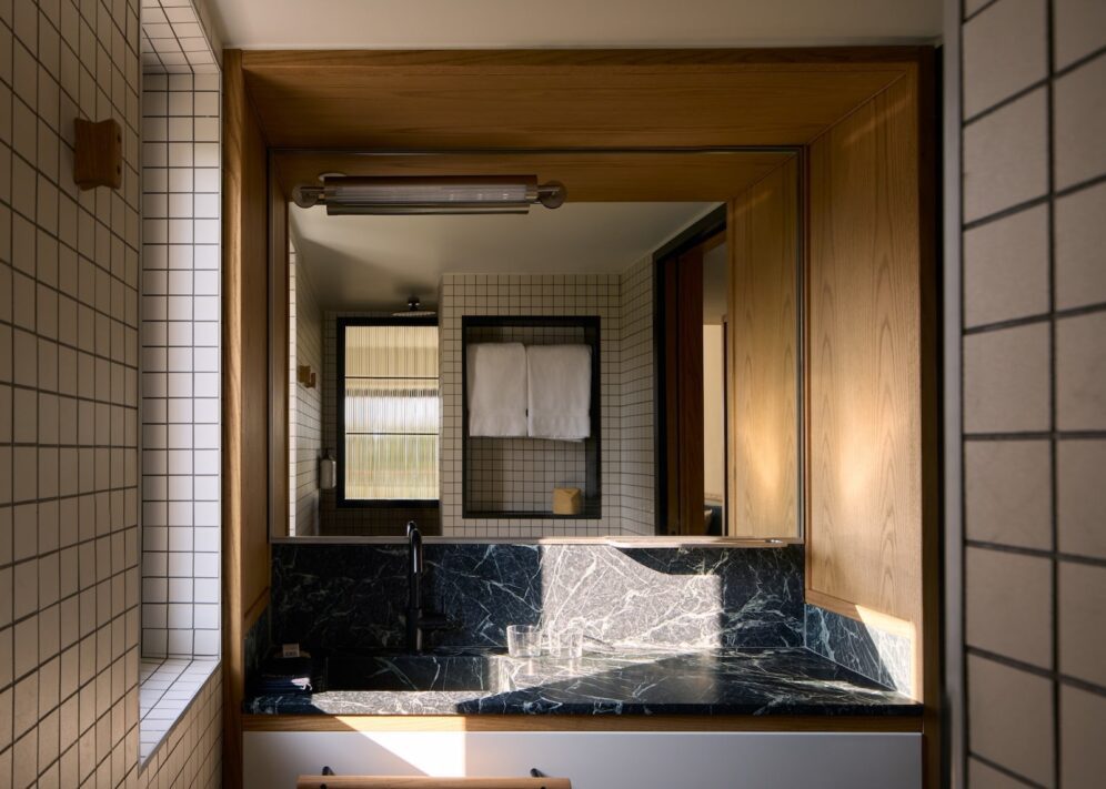 Modern bathroom with wooden accents and grid-patterned white tiles. Features a large mirror, black marble countertop, and neatly hung towels, conveying elegance and tranquility.