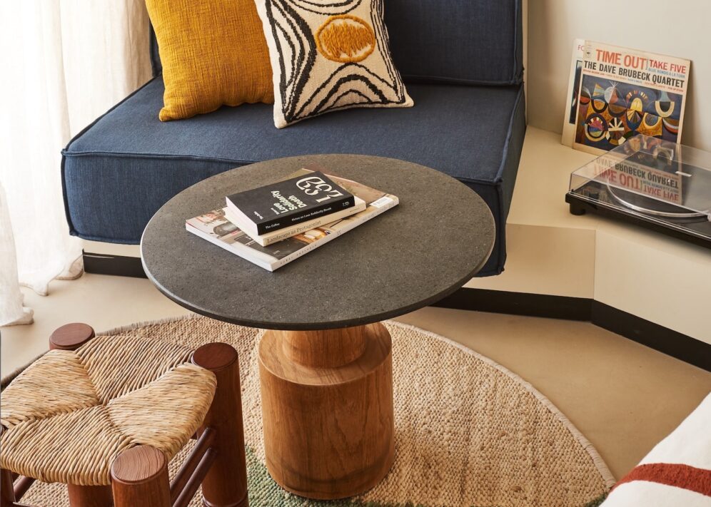 A room featuring a couch, small table, stool, colorful pillow, and a record player.