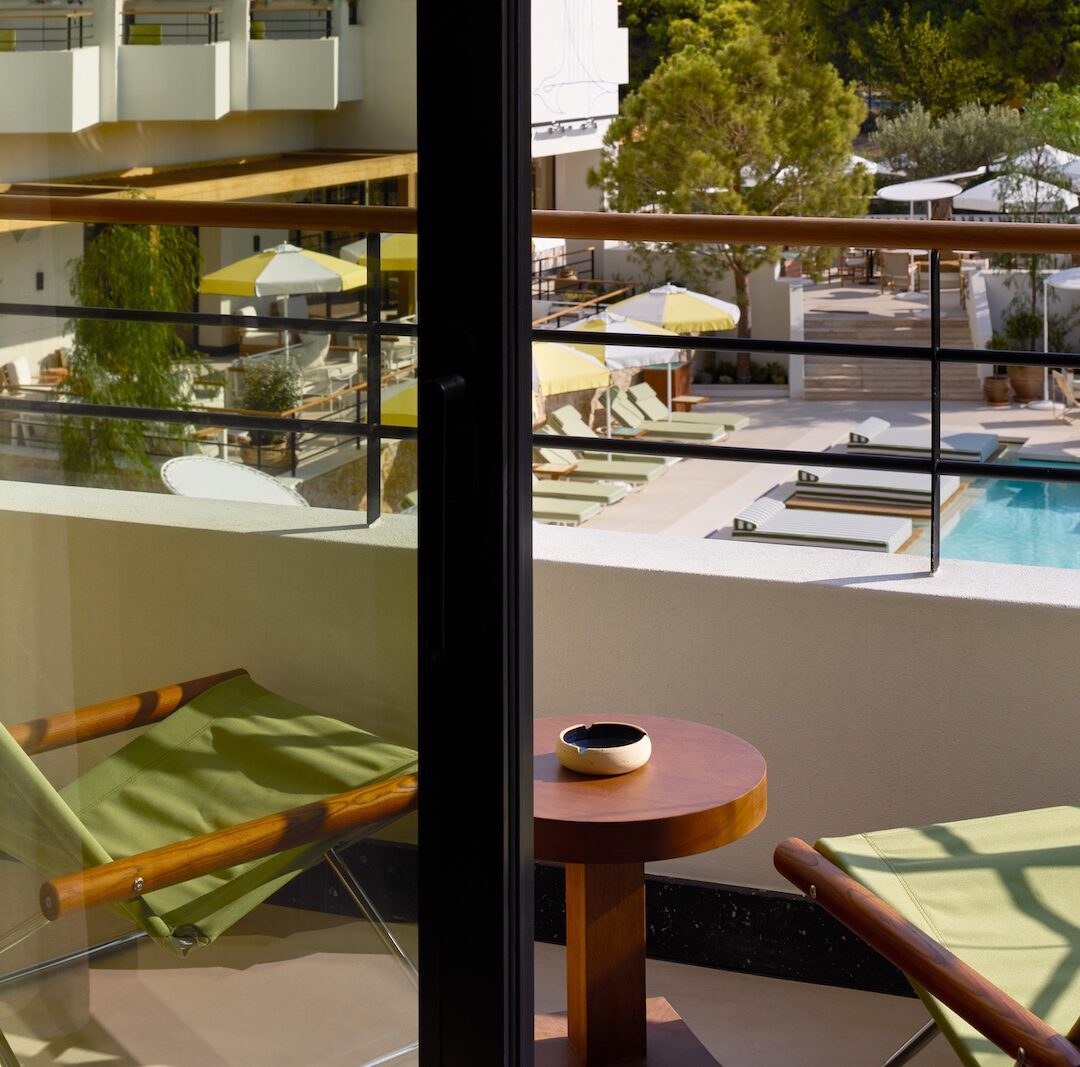 A scenic view of a sparkling pool seen from a cozy balcony, surrounded by lush greenery.