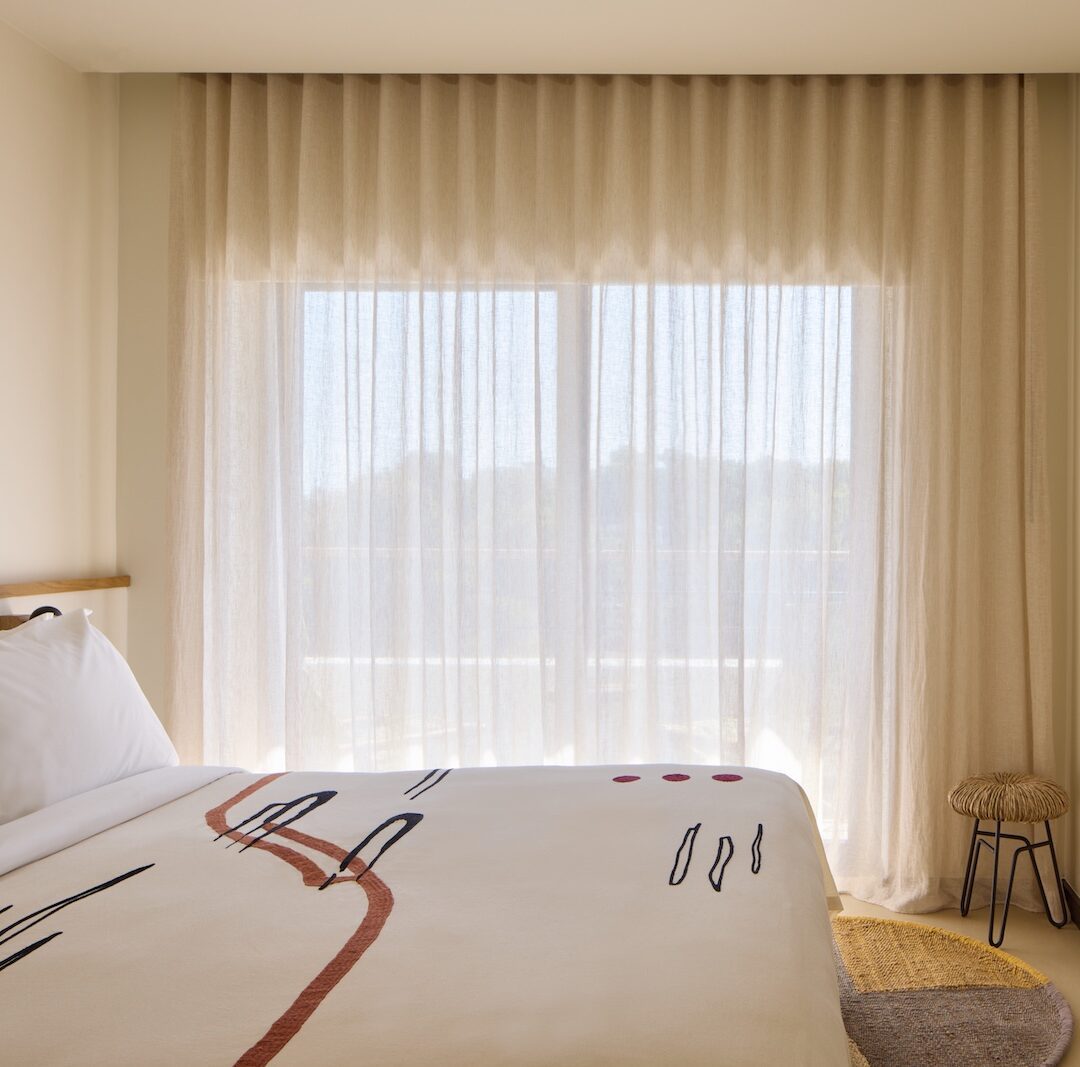 Bright bedroom with a spacious bed, a TV, and tall windows that enhance the airy atmosphere.