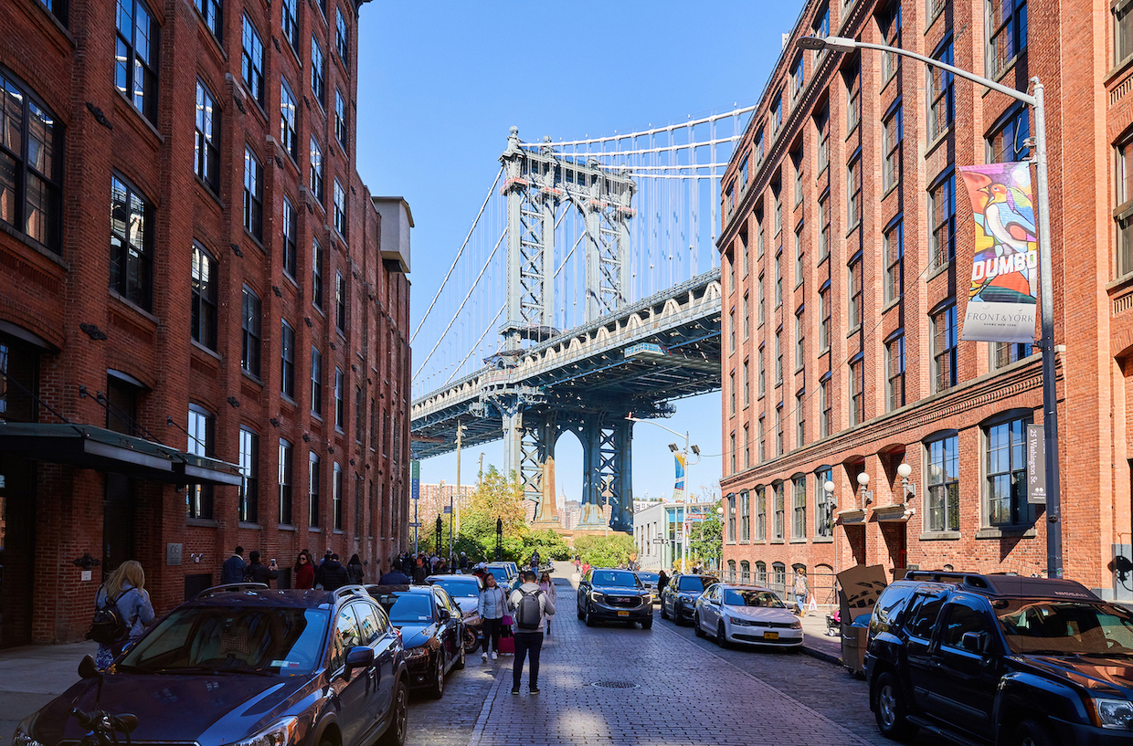 Brooklyn bridge and brick buildings on both sides of the street, parked cars and people walking