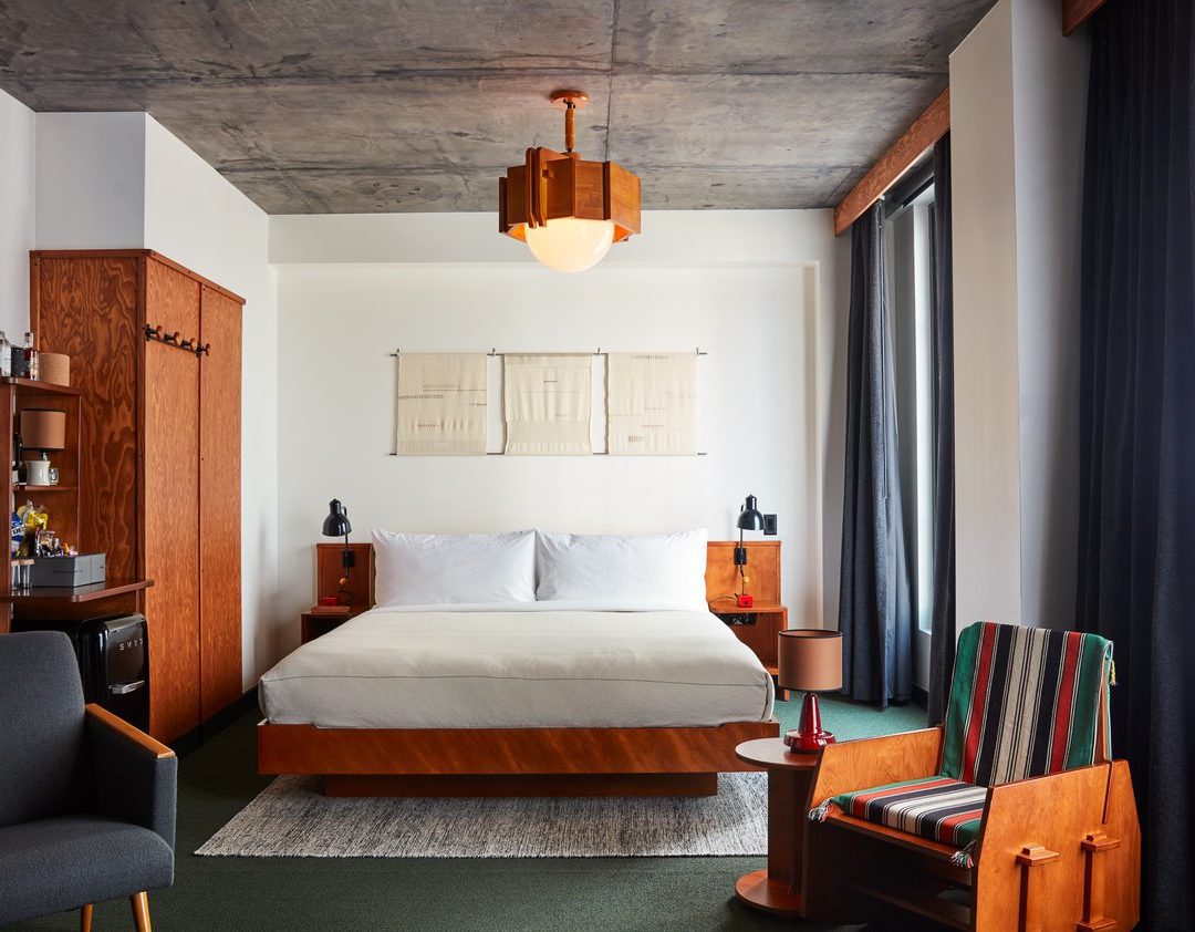 A bed tucked into a corner with bed lamps on each side and a standing closet for hanging clothes