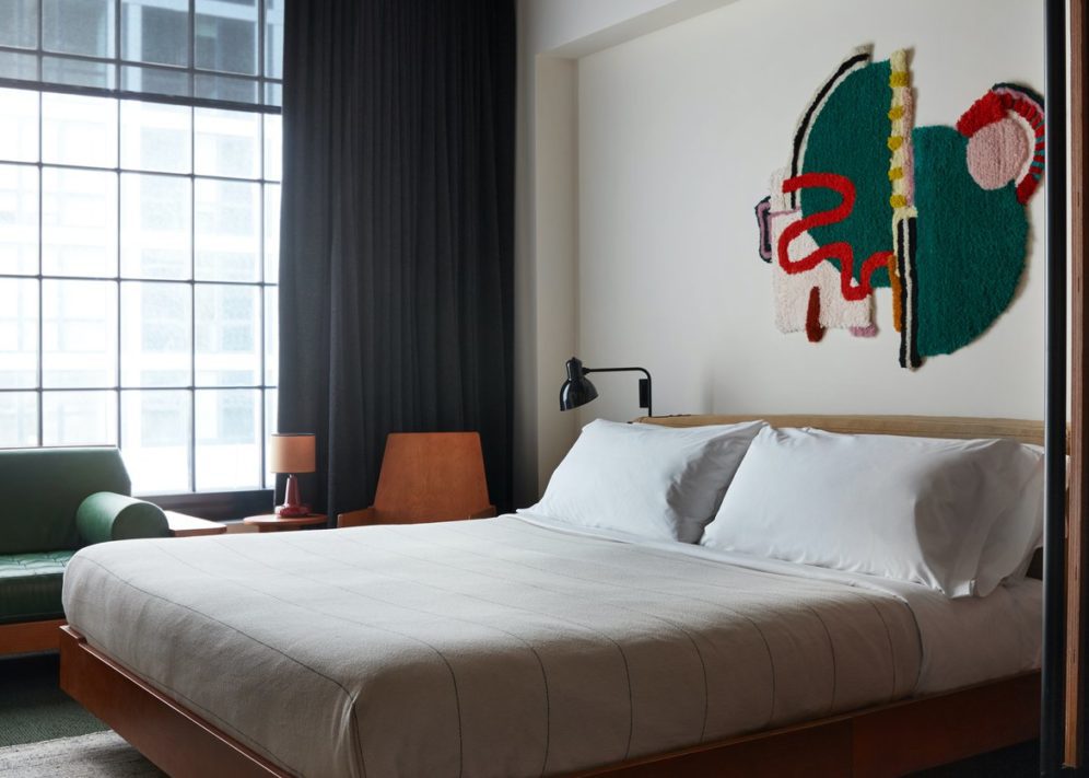 Queen size bed with white linen sheets, green decoration art piece on the wall, a big window