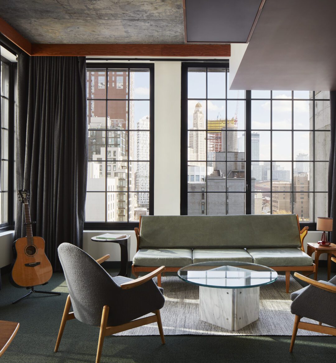 Spacious living space with multiple chairs and a sofa with windows on multiple walls providing sweeping city views