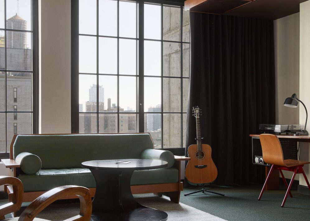 a living room with large windows a table, chairs couch and guitar with a desk