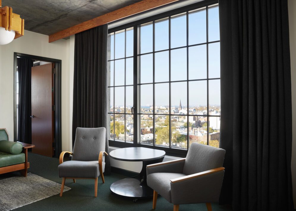 a sitting area with two chairs and a table with a window behind on the one bedroom suite at ace hotel brooklyn