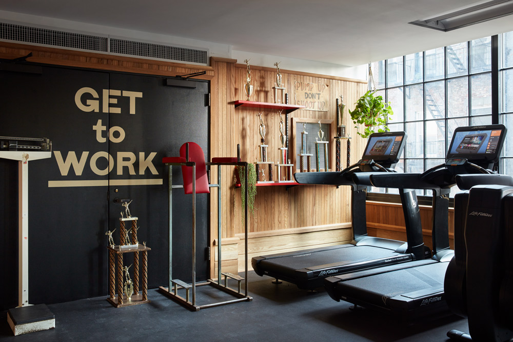 a photo of a gym with equipment that includes dip and leg raise standing machine and manual sliding scale and treadmills. A sign that reads, 'pump up, dont shoot up' and weight lifting trophies.