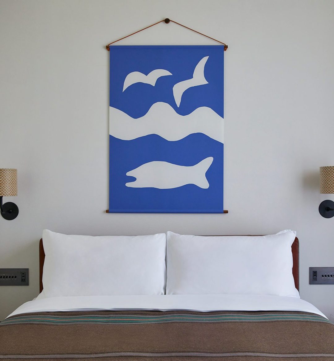 A bed with brown bedding is flanked on either side by stylish wall mounted lamps