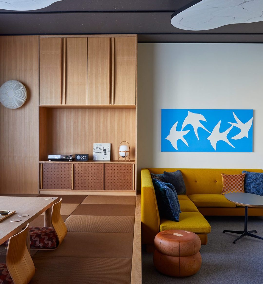 A spacious room is separated into two parts – one area features a stylish yellow couch and more seating, and the other area provides a table close to the floor for tea