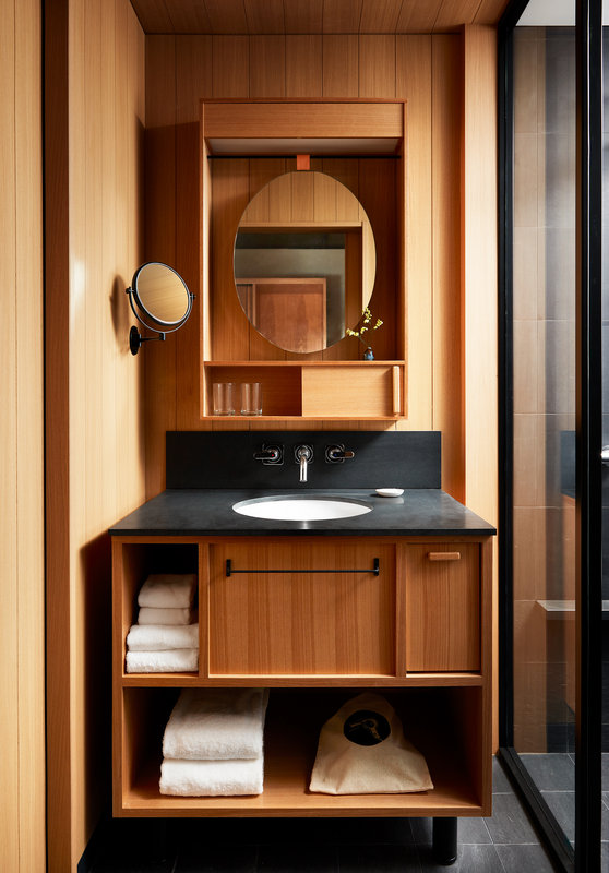 A black stone bathroom sink features two mirrors and stylish wood details