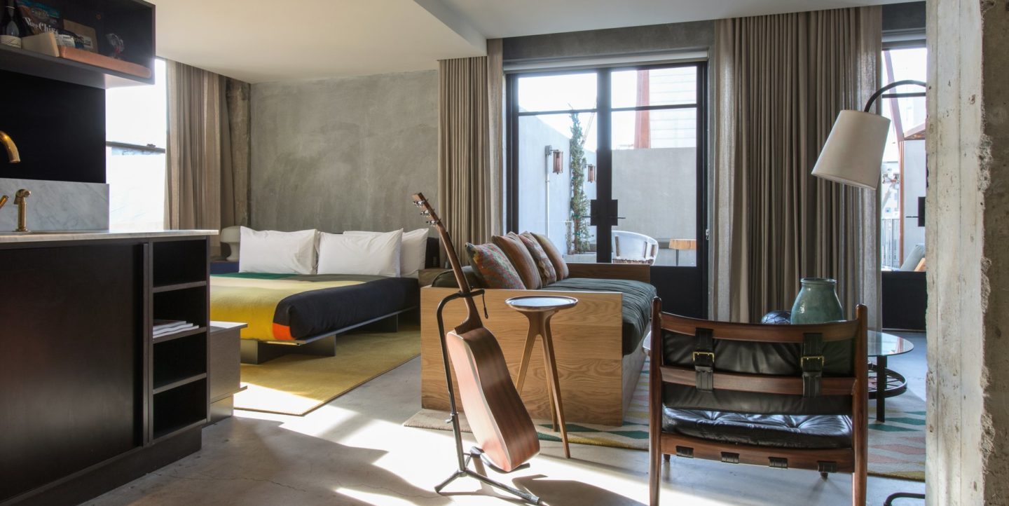 Una habitación de hotel con una cama, un área de descanso, cocina americana y guitarra
