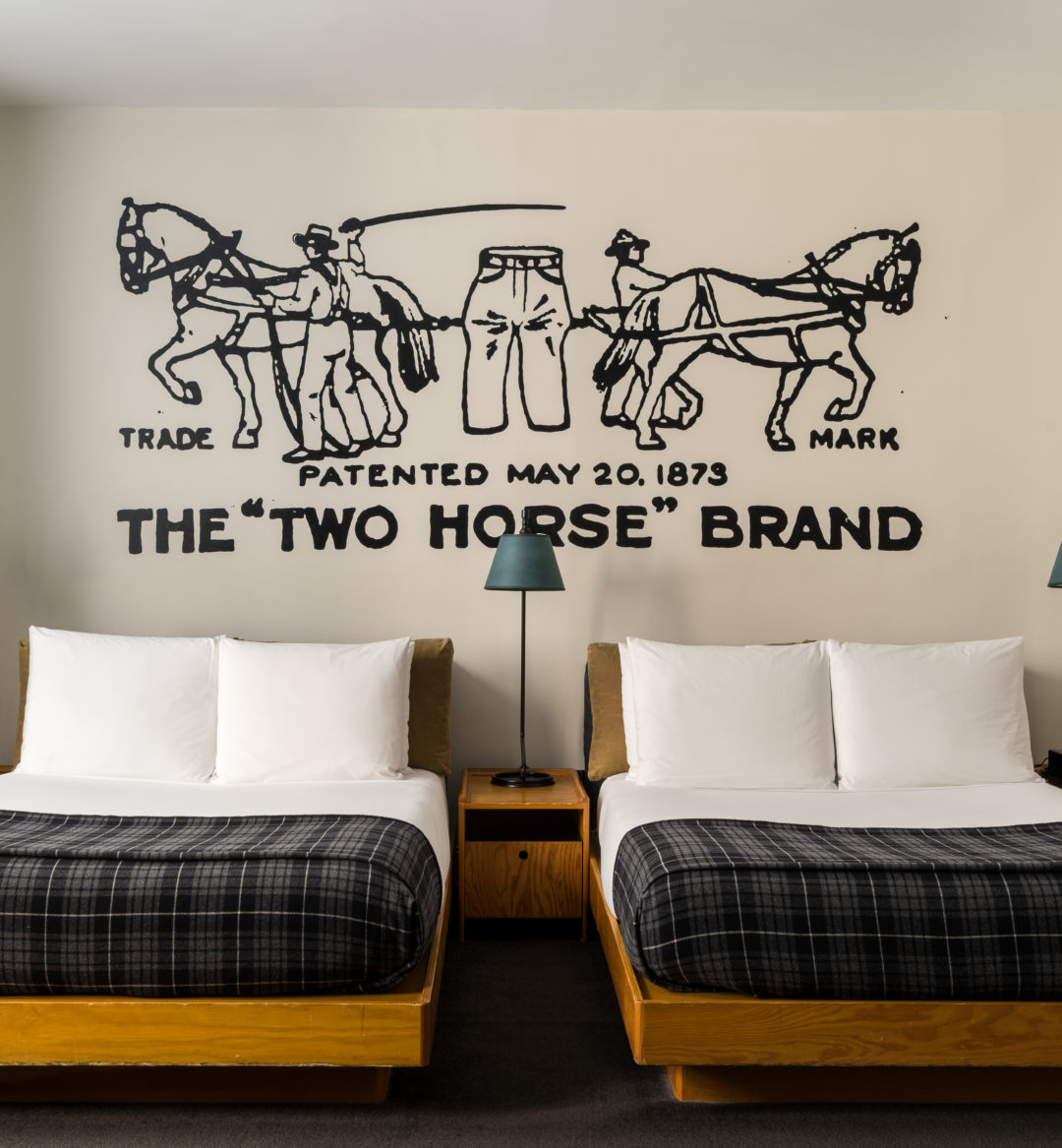 Two beds are flanked on all sides by tall side lamps, and original custom art is painted on the wall above the beds