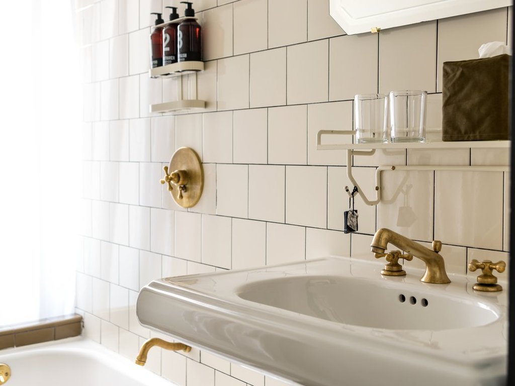 An elegant white tiled bathroom features golden faucets and handles