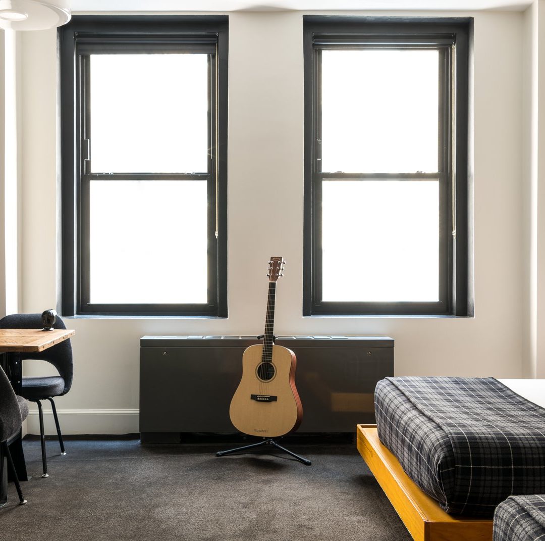 A room with dark carpets features 2 windows and a corner desk with multiple chairs