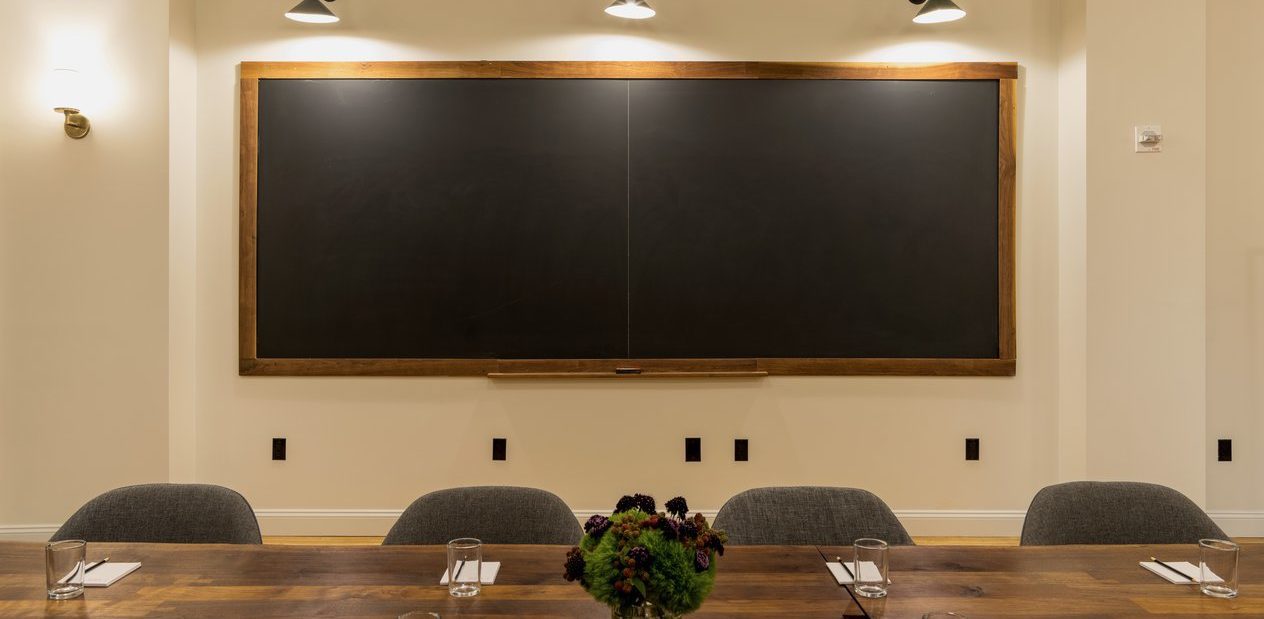 A meeting room with a large table and a chalkboard on the wall