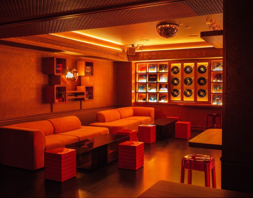 Libera corner sofa dining area with orange lit lights, vinyl record background wall and small tables.