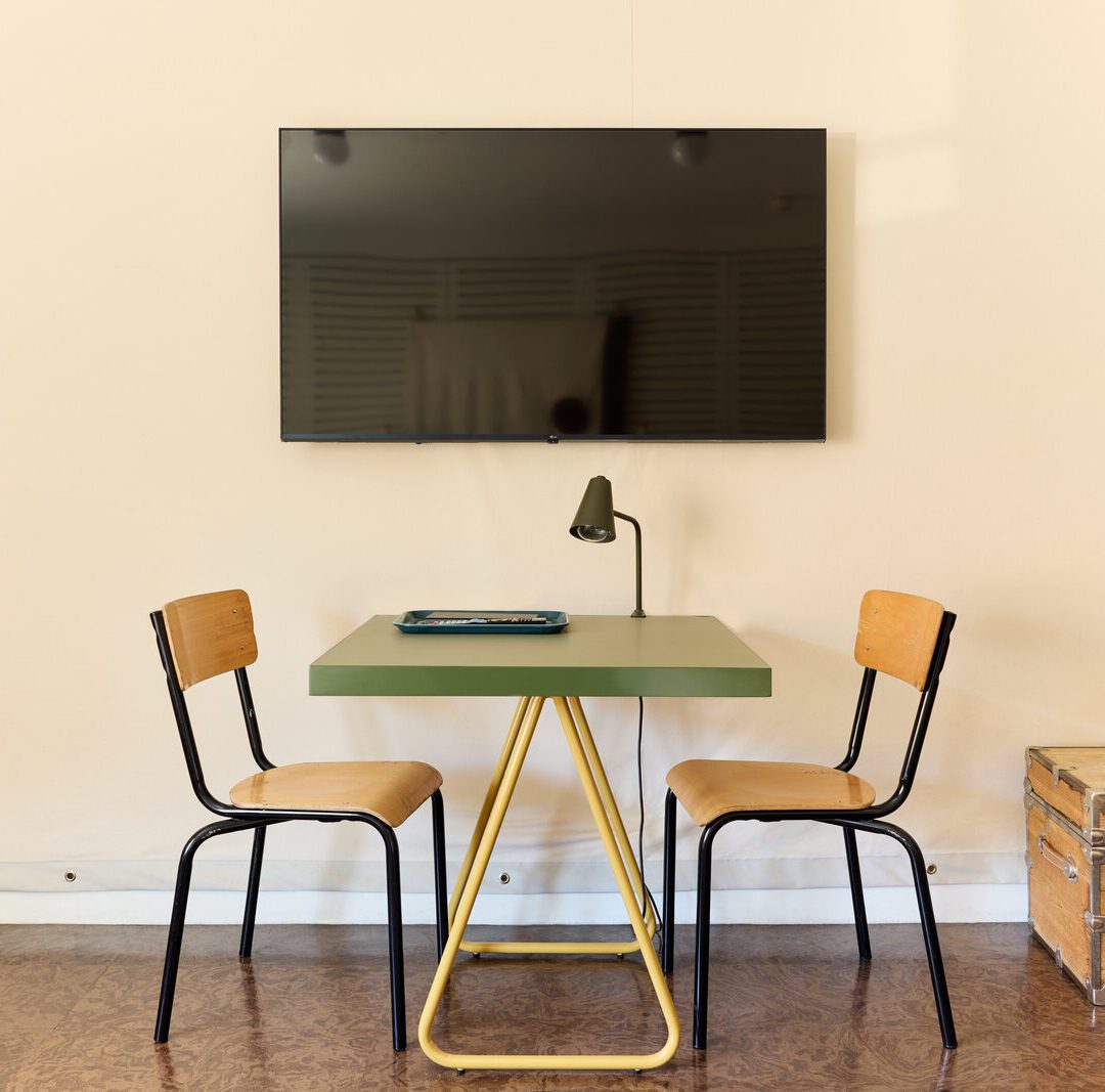 A simple green desk with a reading lamp sits under a television