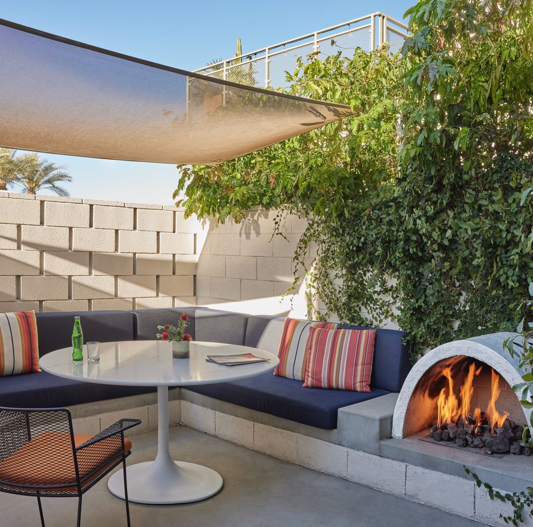 A private patio provides a sofa, table, and chair for outdoor relaxation; a small, semicircular fireplace provides warmth and ambiance
