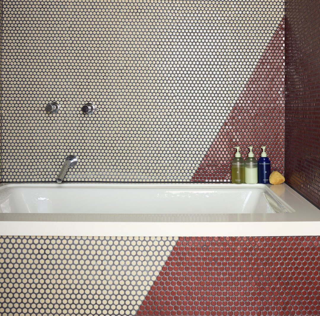 A red and white tiled bathroom features a deep bathtub