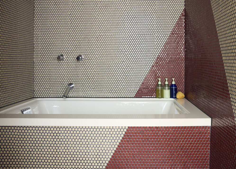 A red and white tiled bathroom features a deep bathtub