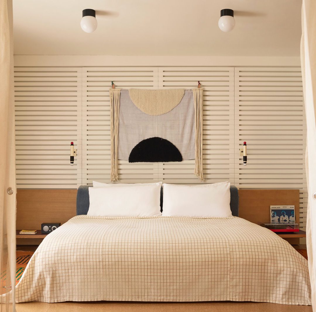 A private bedroom features a white, plaid bed flanked by a record player on one side and a radio and phone on the other