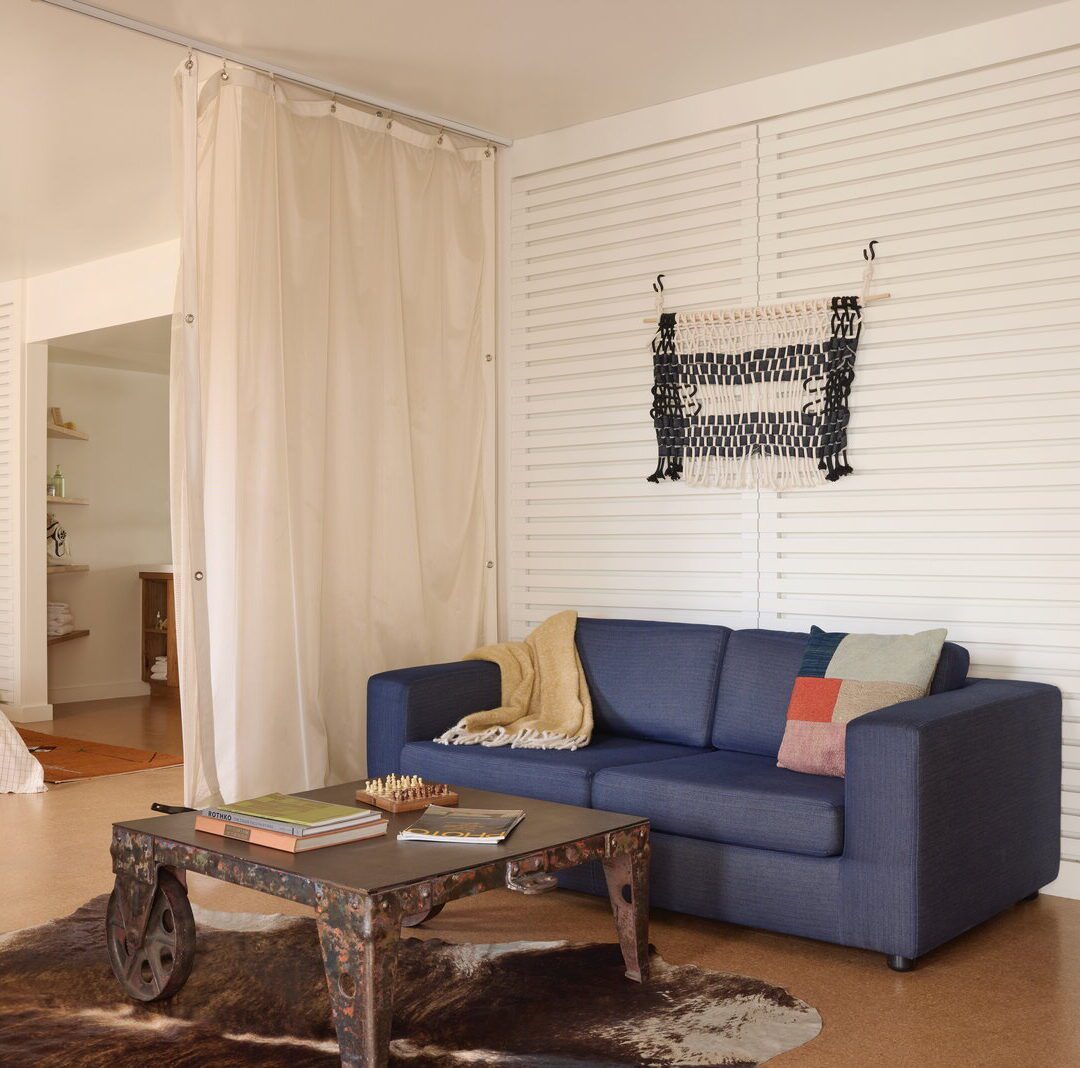 A blue sofa and rustic coffee table provide a place to sit and relax; a curtain separate the living room from the bedroom