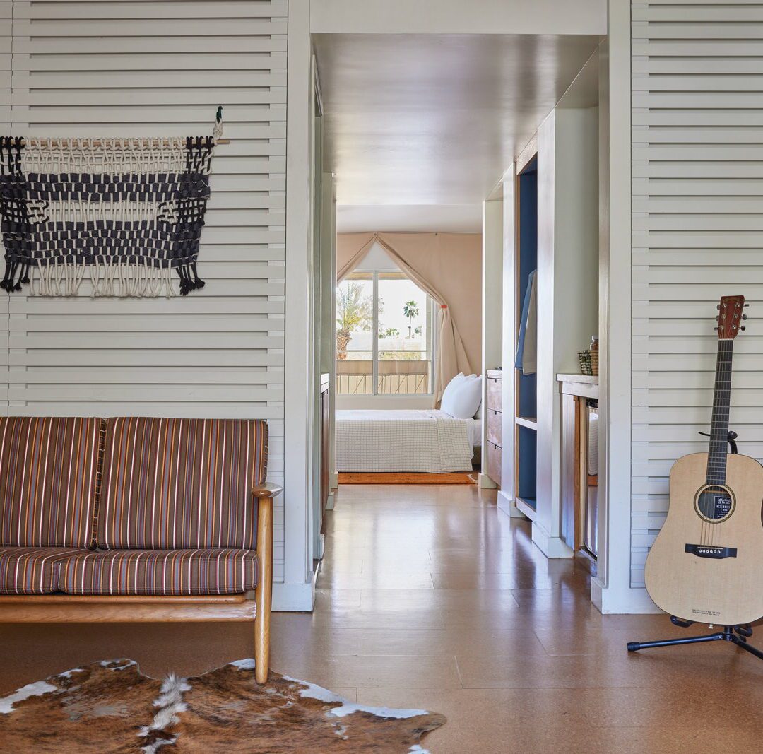 A small couch sits in front of an animal skin rug; a hallway leads to a bedroom with natural light