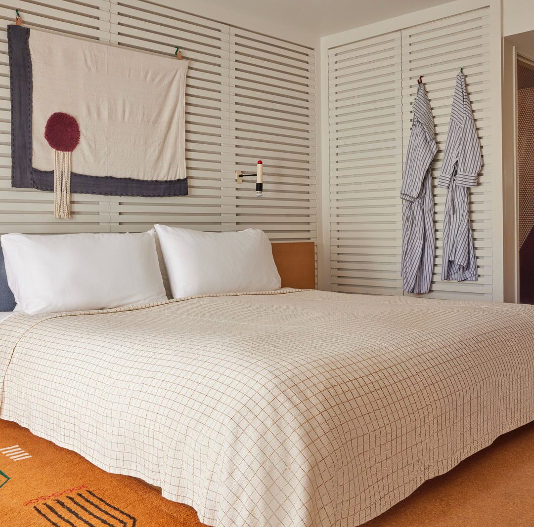 A bed with plaid bedding is drenched in natural light and an ornate brown rug adorns the floor