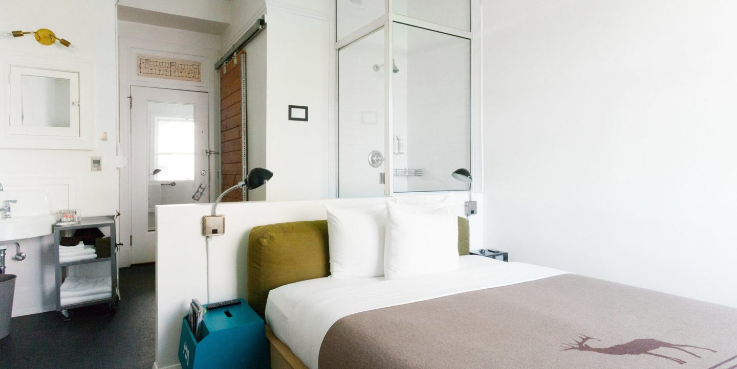 A hotel room with a twin bed, shower, and sink