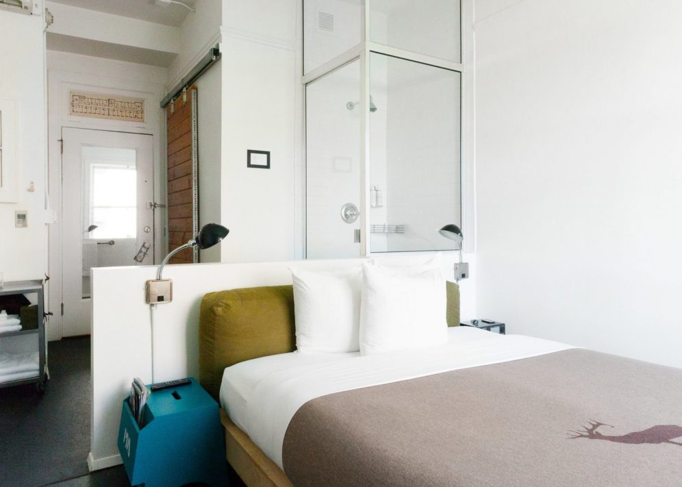 A hotel room with a twin bed, shower, and sink
