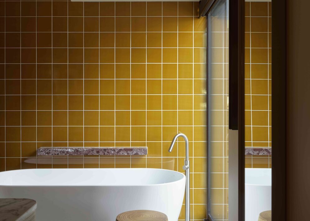 A yellow wall tiled bathroom features a standalone bathtub