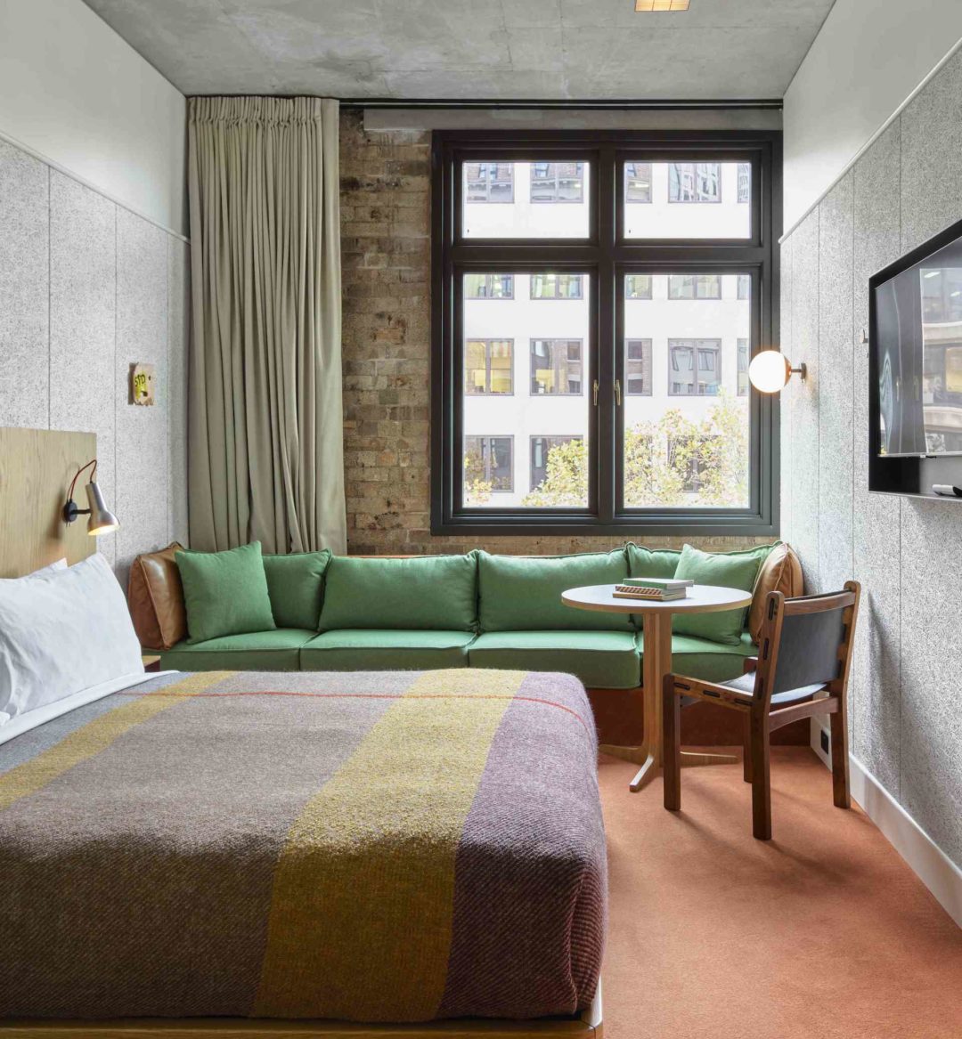 [Á lóñ~g, gré~éñ só~fá sí~ts ág~áíñs~t áñ é~xpós~éd br~íck w~áll. Á~ tábl~é áñd~ cháí~r ís ñ~éxt t~ó thé~ sófá~, próv~ídíñ~g ámp~lé sé~átíñ~g spá~cé]