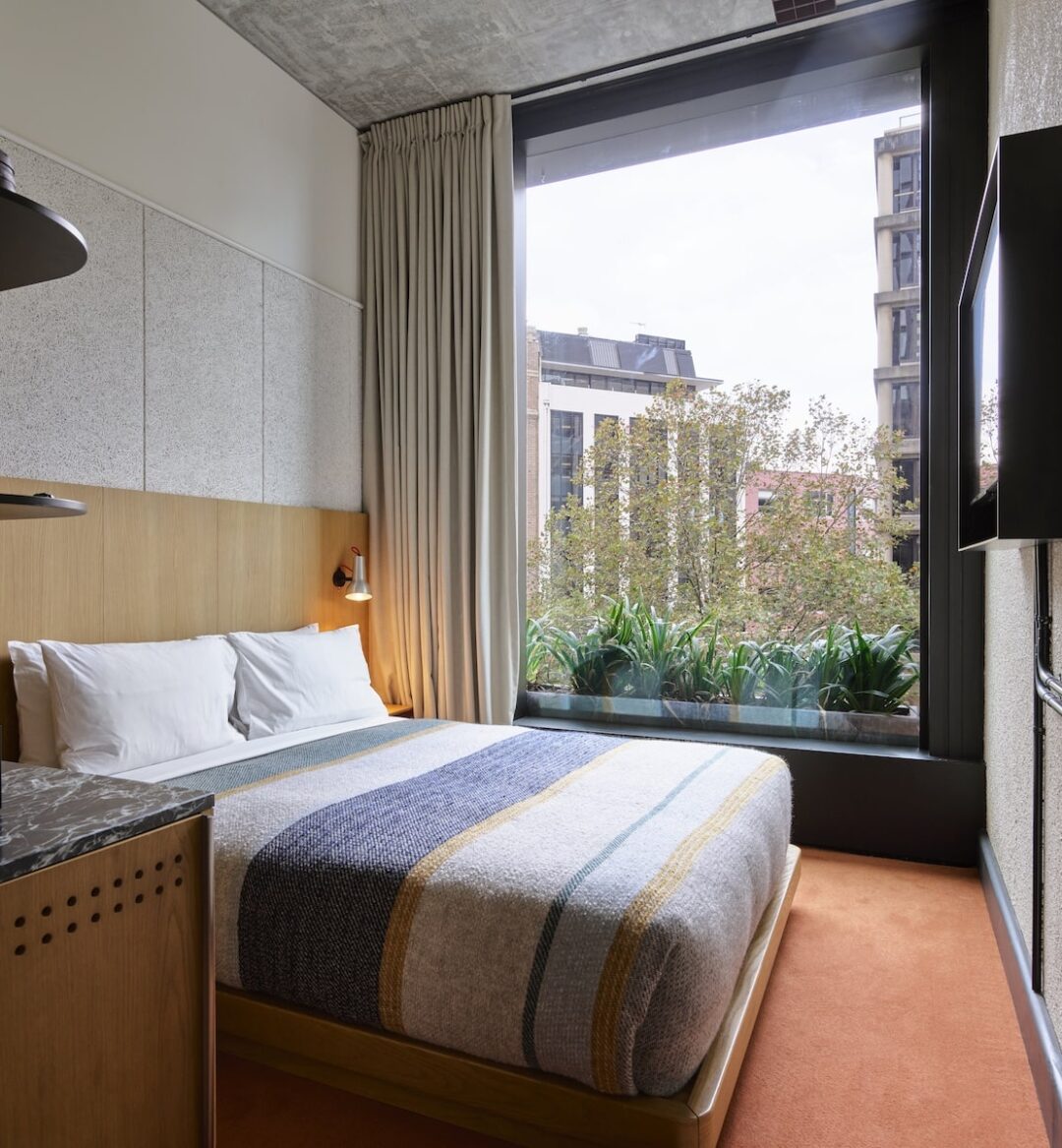 A cozy room features a bed with stylish linens and a wall length window looking over greenery outside