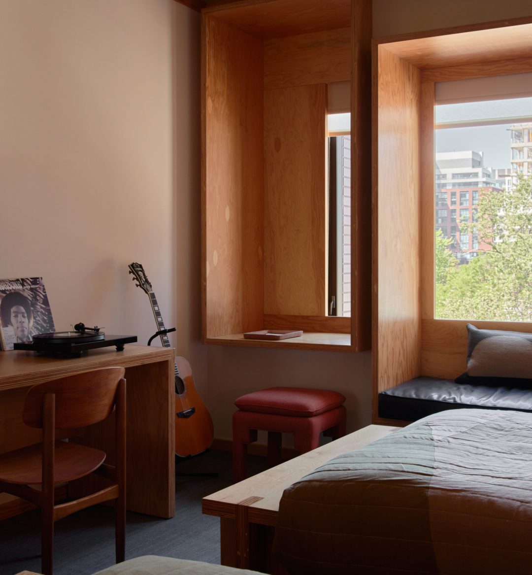 A record player and records sit against a window; a red footstool sits on the floor
