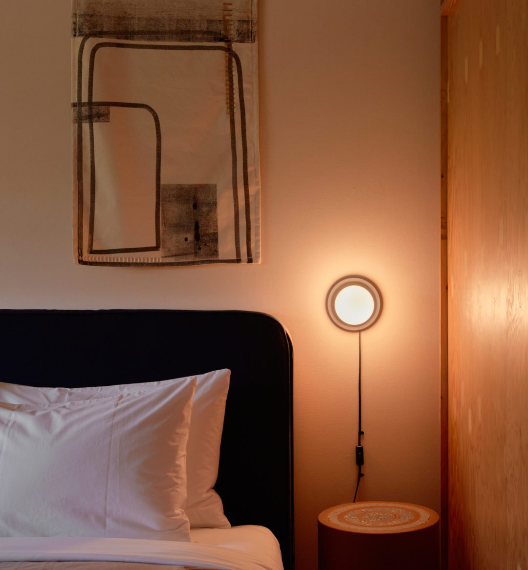 A modern mounted wall light sits next to a bed, providing an opportunity for late night reading