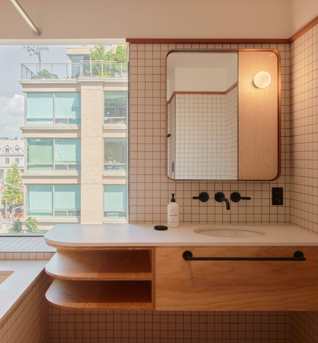 A modern white tiled bathroom features a spacious vanity area and large window