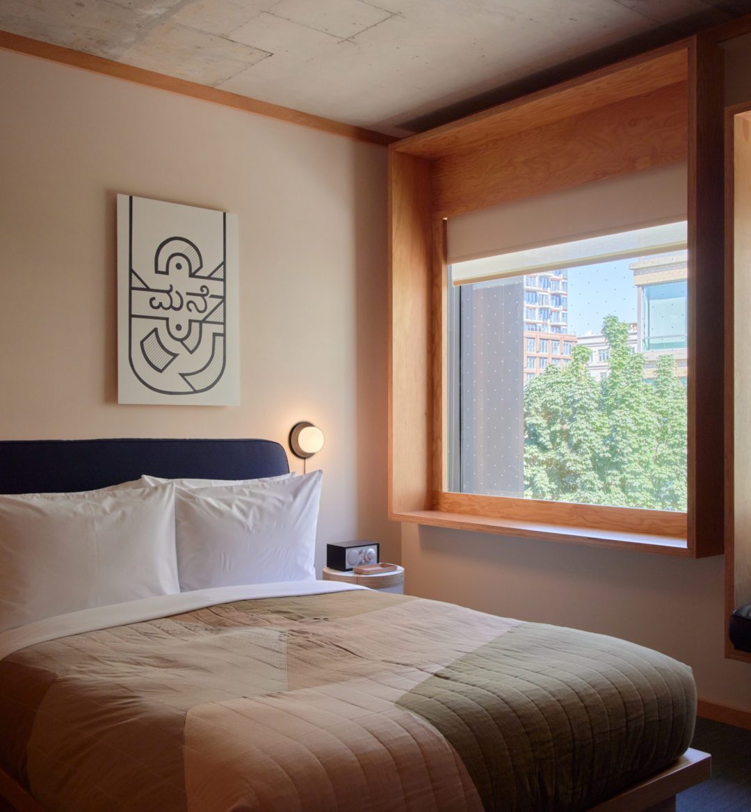 A bed sits next to a wall featuring two windows and a black leather seating area