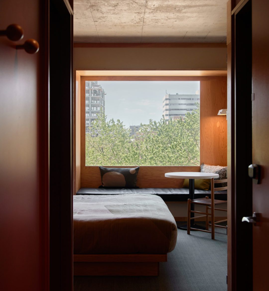 A wood paneled room features a black leather seating area under a window featuring greenery