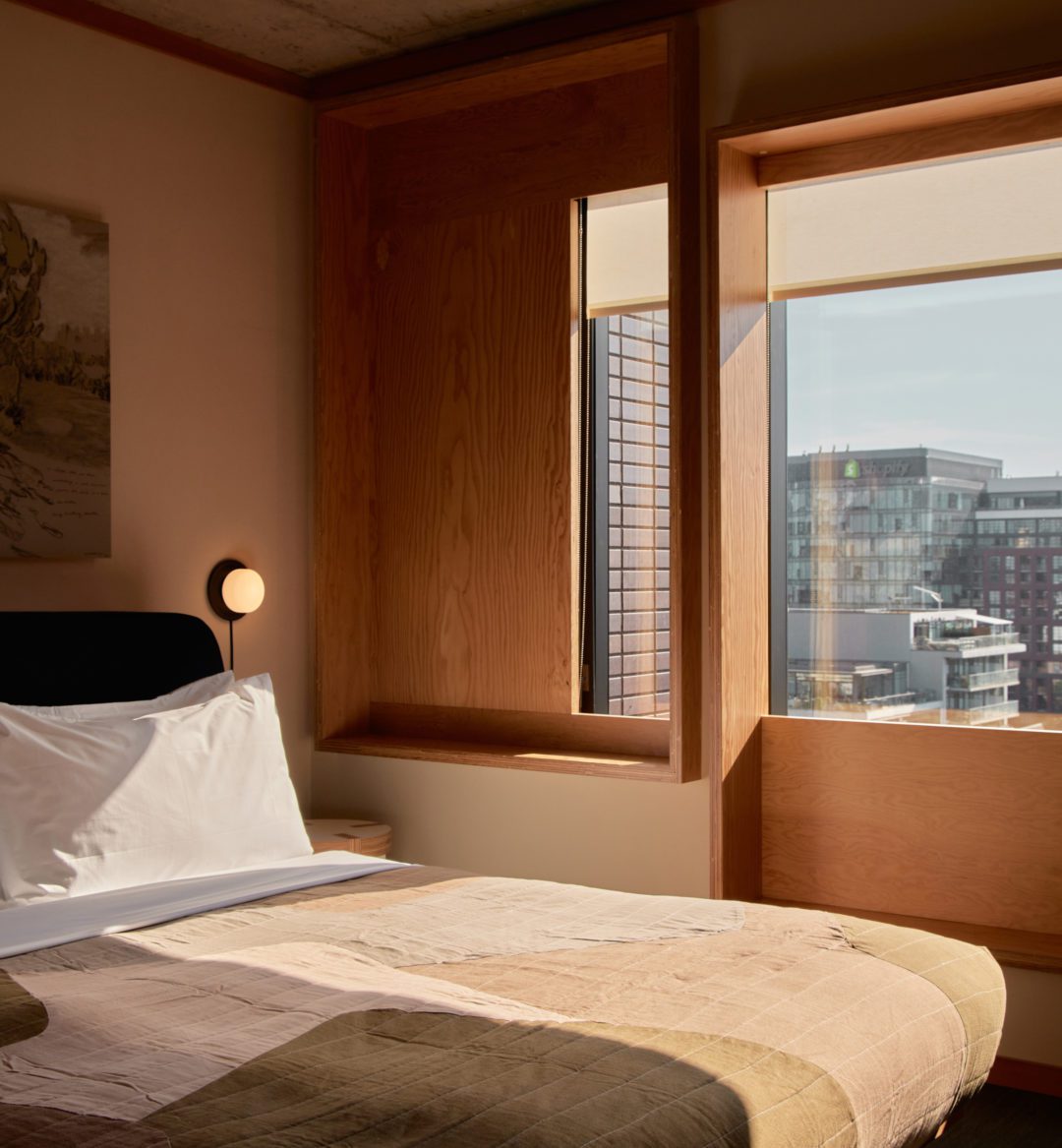 A bed sits next to two windows, offering expansive views of the city