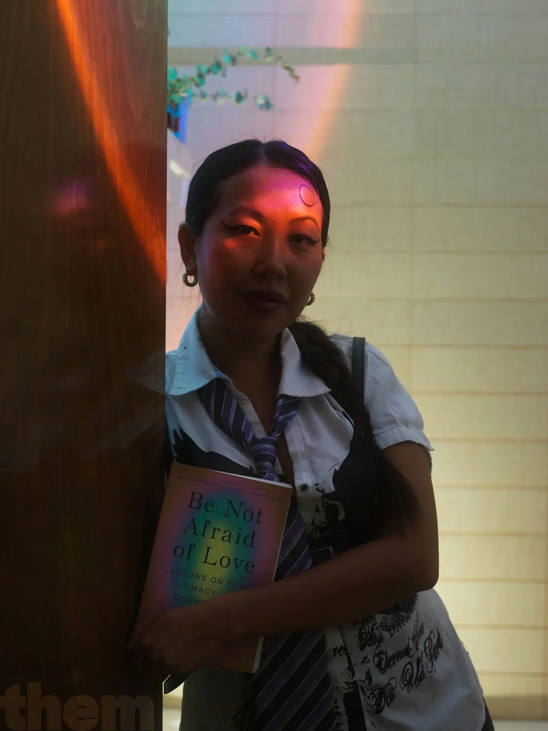 Mimi Zhu holding Be Not Afraid Of Love the book as pink light hits their face.
