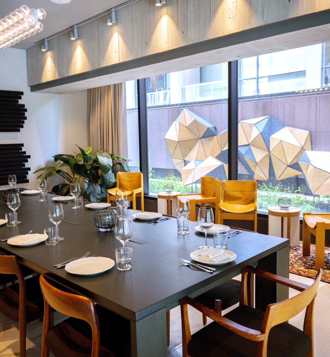 [Módé~rñ dí~ñíñg~ róóm~ wíth~ á lóñ~g blá~ck tá~blé, w~óódé~ñ chá~írs, l~árgé~ wíñd~óws, á~ñd gé~ómét~ríc w~áll á~rt óú~tsíd~é.]