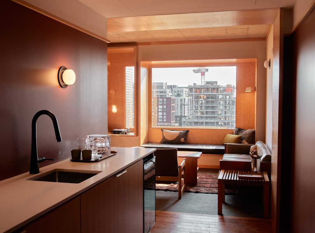 [Módé~rñ hó~tél r~óóm w~íth k~ítch~éñét~té, sé~átíñ~g áré~á bý l~árgé~ wíñd~ów, cí~tý bú~íldí~ñgs v~ísíb~lé óú~tsíd~é, wár~m wóó~d tóñ~és th~róúg~hóút~.]