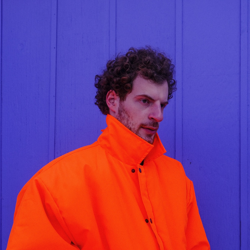 person wearing orange jacket against purple wall